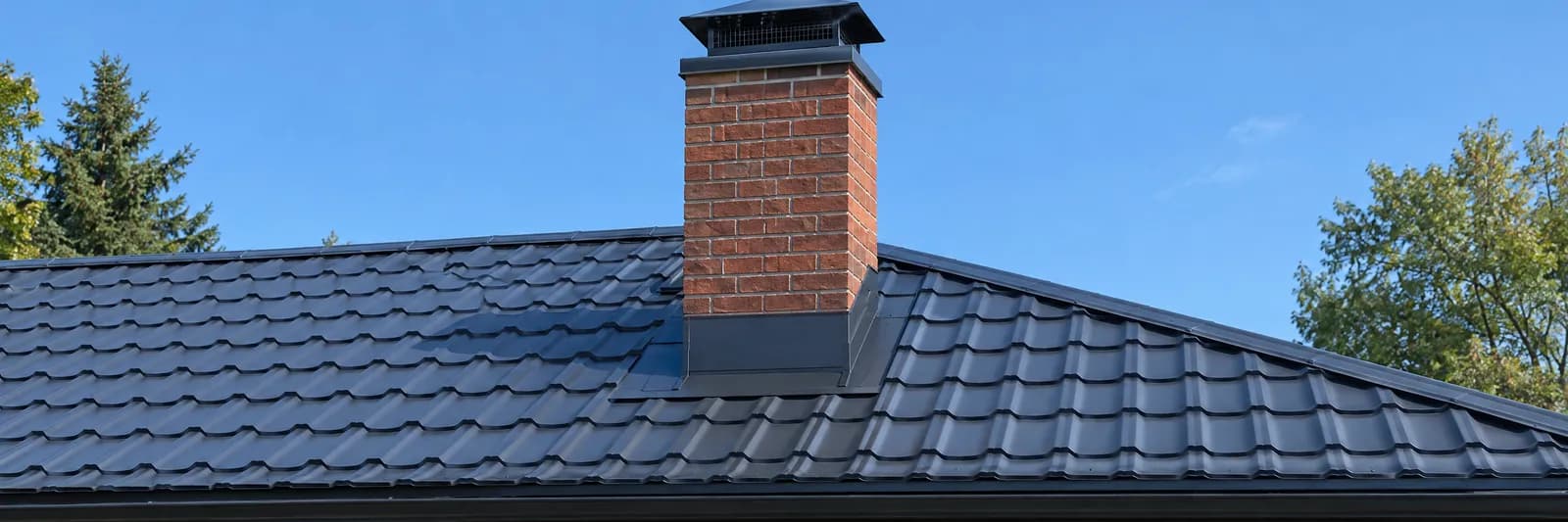 A brick chimney flashed into a dark metal roof with a chimney cap on top
