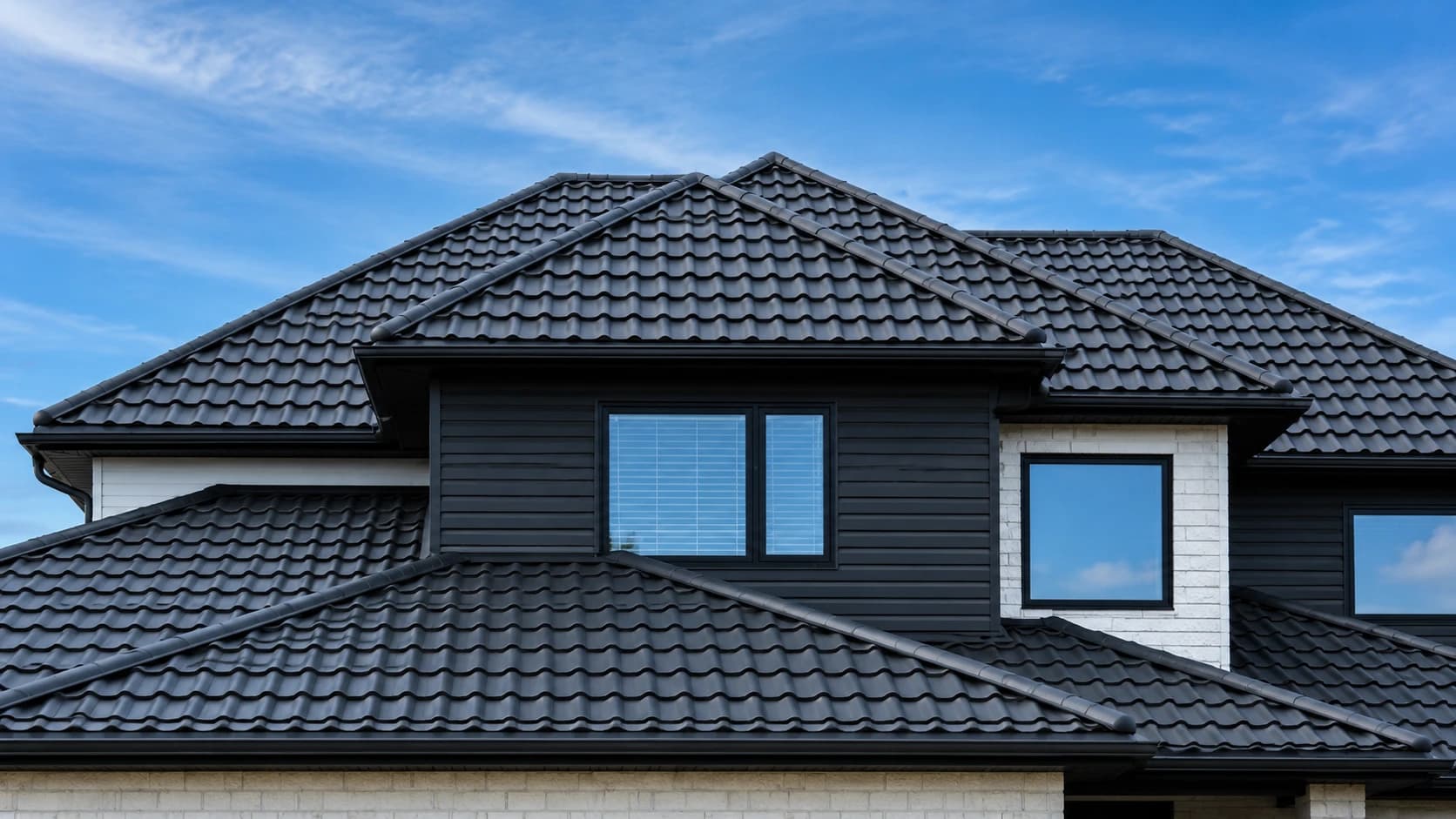 Black Tremblant metal tile roof on a two-storey house against a blue sky